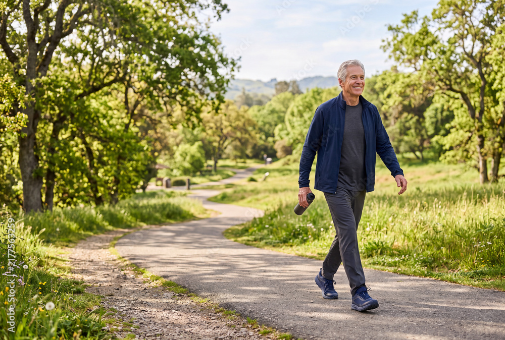 Fototapeta premium Active senior man enjoying a peaceful walk through a green park surrounded by trees, fresh scenery and natural landscapes.