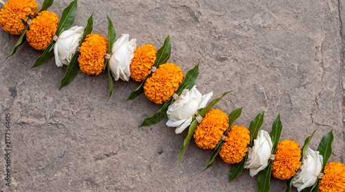 Handcrafted diagonal garland of orange marigold and white flowers arranged on a textured gray stone background, traditional Indian decoration.