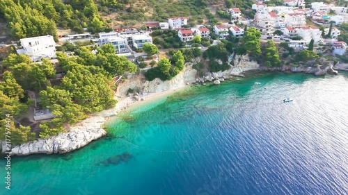 Drone view of an Adriatic coastal town with turquoise sea, green hills and a beach.