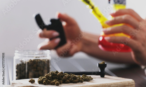Obraz na płótnie Girl Lights A Smoking Bong With Dry CBD Cannabis And Exhales Thick Smoke For Cal