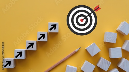 Wooden blocks with arrows pointing towards a bullseye target with a dart on a yellow background, for business goals