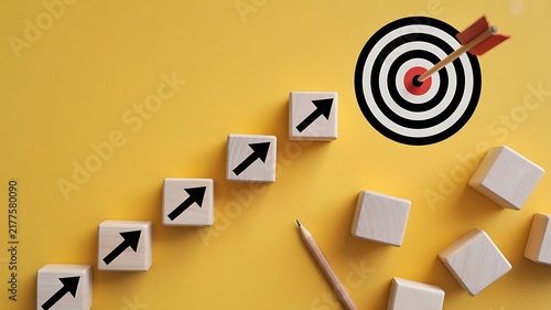 Wooden blocks with black arrows pointing towards a target with an arrow in the center on a yellow background surface