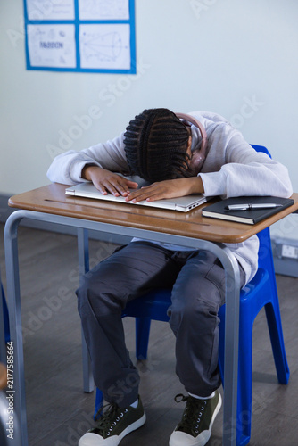 Canvas Print Teenage African-American girl slumping, resting head on closed laptop with pink