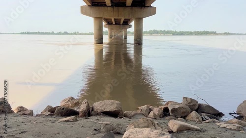 view of a wide river flowing peacefully beneath a sturdy bridge in a scenic rural landscape. 4k video