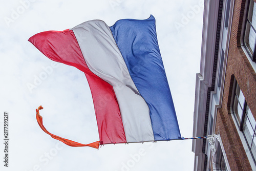 tricolor Dutch flag in red, white, and blue with orange ribbon at top, flying on King's Day