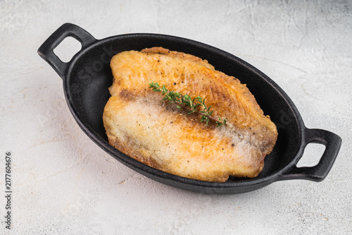 Fotografie Pan fried tilapia fillet served in small cast iron skillet with thyme on wooden board over light background with copy space