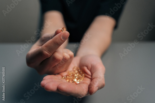 Fotografie Person holding gelatin capsules and showing one capsule between fingers, concept health, wellness, pharmaceutical treatment option, emphasizing medical care, vitamin intake