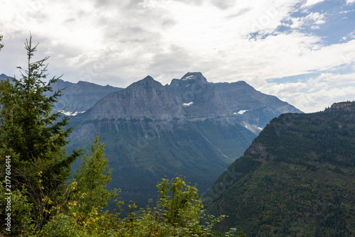 Фотография High above the road, the mountains around Logan Pass create a wild alpine panorama where rocky peaks, lingering snow, and shifting clouds meet