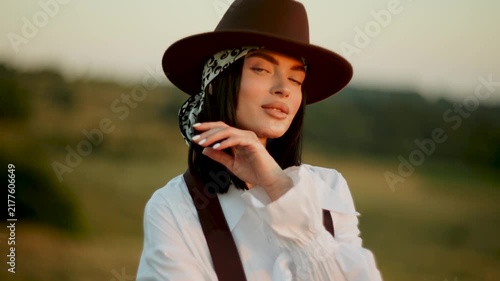 Young woman in a brown hat poses in a peaceful field during the golden sunset hour in California