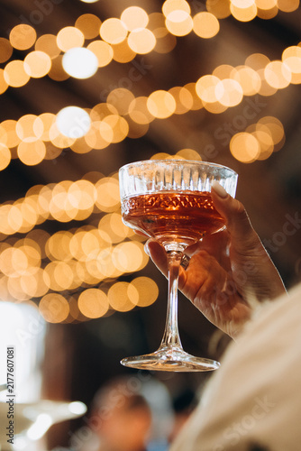 Hand holding cocktail glass celebrating event with bokeh lights
