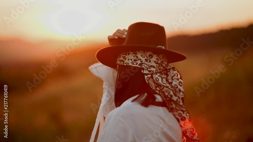 Woman holding a hat while standing in a field during a warm golden sunset in the countryside