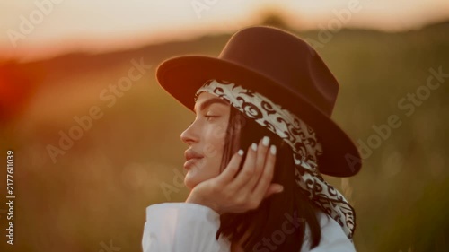 Woman in hat poses during golden hour sunset in a grassy field meadow