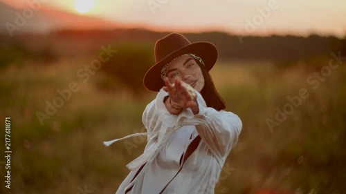 Woman in a hat walks through a golden field at sunset