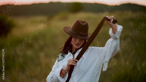 Woman wearing a brown hat and white shirt posing in a grassy field during the golden hour