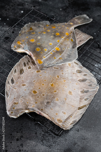 Fotografía Raw flounder flatfish with spotted skin on rack with pepper on dark background f