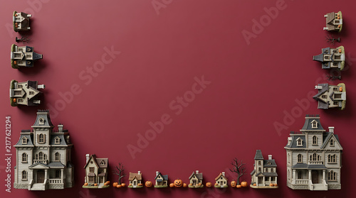 Miniature haunted houses and spooky village buildings arranged as a decorative frame on a dark red background