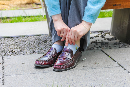 Warsaw, Poland, May 15, 2026. Close up of woman tying laces on burgundy leather shoes sitting on park bench outdoors. High quality photograph