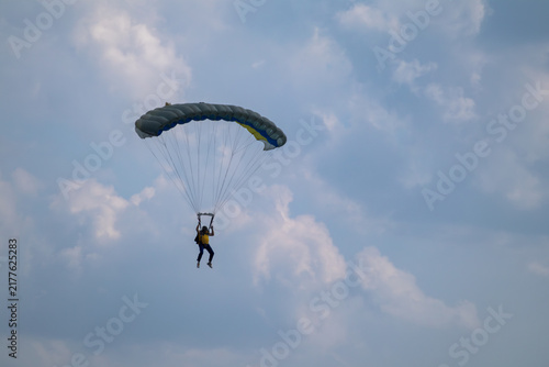 Foto Parachutist descends through a scenic cloudy sky under a yellow and blue parachu