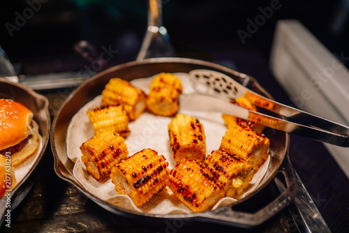Foto Grilled corn on the cob pieces arranged in a metal serving tray with tongs, show