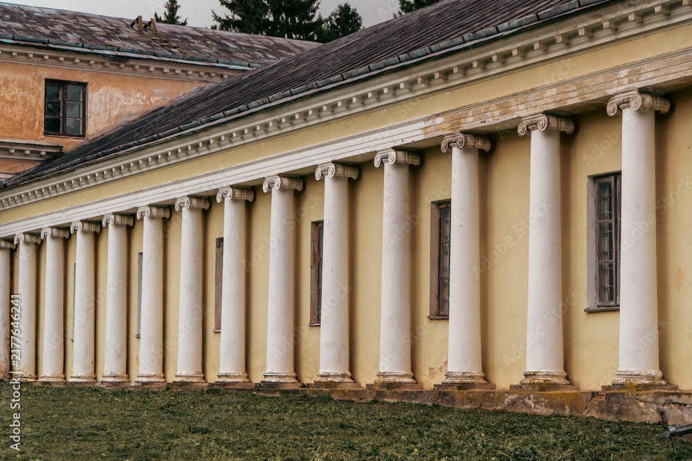 Fototapeta premium A long neoclassical yellow building features a rhythmic colonnade of white ionic columns standing along a grassy lawn.