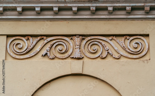 Decorative classical bas-relief scrollwork with acanthus leaves and spiral ornaments adorns the beige stucco facade of a historic building.