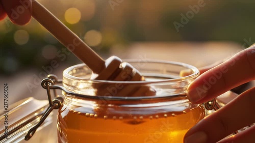 Hand using wooden dipper to scoop and drip golden honey into glass jar. Food industry, natural sweetener, healthy eating, cooking, dessert.