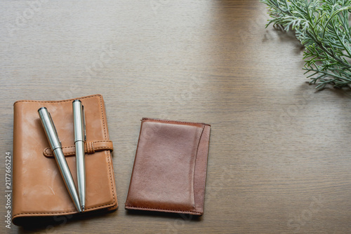 Fotografía Camel leather notebook, silver pens and a brown leather cardholder on a wooden desk with plenty of copy space