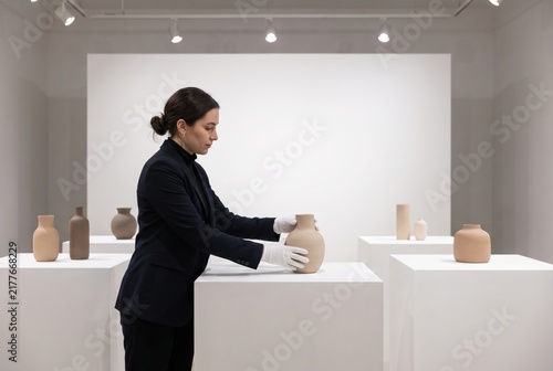 Female gallerist arranging a ceramic vase on a white pedestal in an art exhibition space