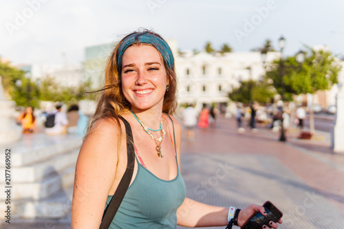 Young woman smiling, enjoying a summer day in the city, feeling happy and free during her urban travel adventure, wearing a headband and stylish necklaces