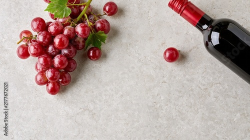 Red grapes and a dark wine bottle arranged on a light stone surface with spacious central copy space