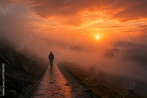 Solitary hiker walking along misty path at sunrise over landscape