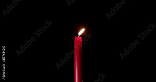 Lit red candle standing alone in a vast and dark space. The moving flame of this beautiful candle creates a mystical atmosphere. A quiet burning candle for soul, prayer, or holiday overlay.