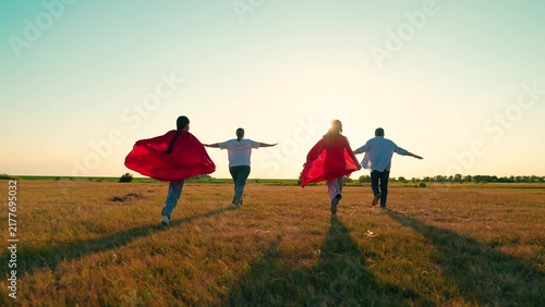 Konstfotografi Happy children, parents playing superheroes, running sun field in red capes