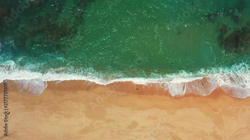 Top down drone perspective of Atlantic surf rolling onto an empty golden sandy beach along the Portuguese coast.