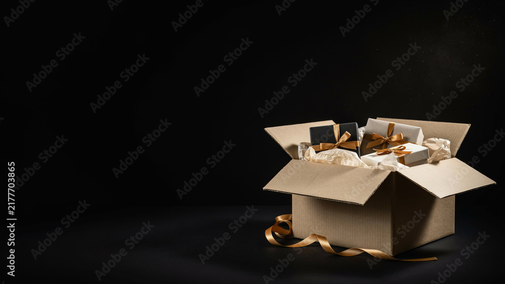 Fototapeta premium A cardboard box overflowing with beautifully wrapped gifts and golden ribbon, set against a dark background.