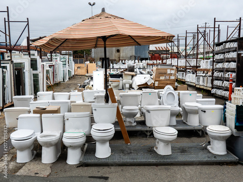 Foto toilets-An outdoor salvage yard displays a large collection of used white toilets arranged beneath a large striped umbrella