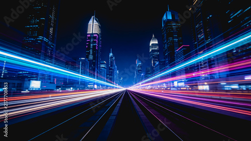 A long-exposure shot capturing vibrant light trails moving along urban tracks through a modern night cityscape of skyscrapers.