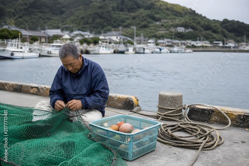 漁港で網を繕う漁師