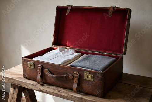Open vintage leather suitcase with folded shirts and blanket, travel and nostalgia concept
