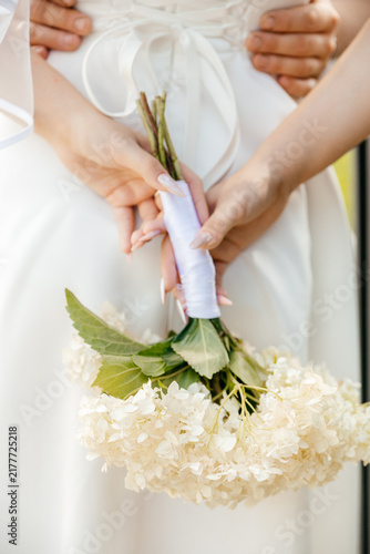 A close-up of two hands holding a bouquet of white flowers. One hand is adorned with a ring, while the other is gently grasping the bouquet's stem.