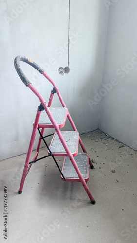 фотографія A pink step ladder stands in an empty room with bare walls and a dusty floor