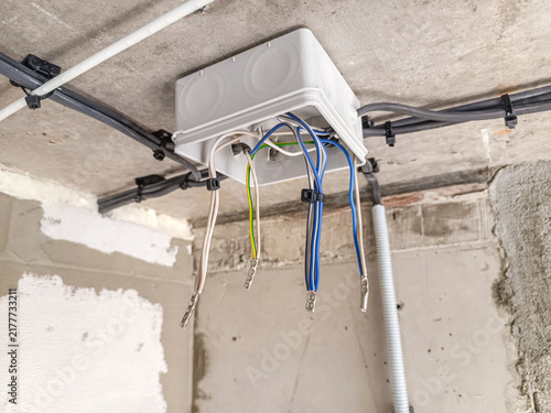 Electrical junction box with multiple colored wires attached to the ceiling. The setting is an unfinished room with exposed walls and ceiling.