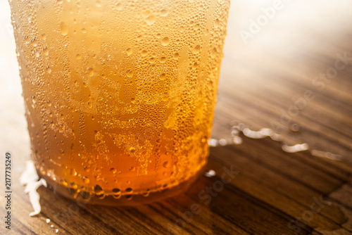 Close up of iced tea or amber beverage with condensation droplets on a wooden table.A refreshing close-up macro shot of a cold amber-colored beverage, such as iced tea, craft beer, or apple juice