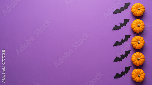 Halloween background with orange pumpkins and black bats on a purple surface