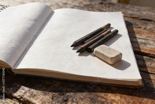 Open sketchbook with charcoal pencils and eraser on weathered wooden surface