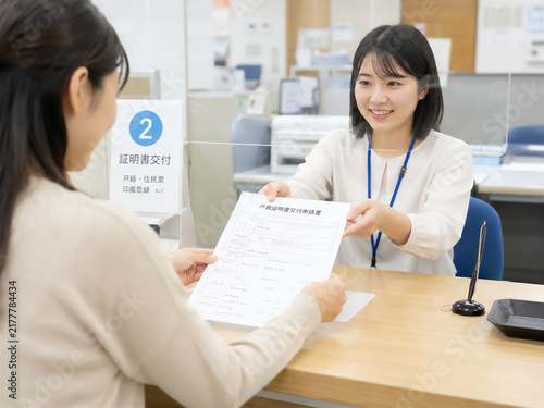 市役所の証明書交付窓口で戸籍関係書類を受け取る女性のイメージ