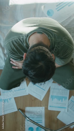 Man overwhelmed sitting on bed with scattered financial papers on floor, top view ,vertical video