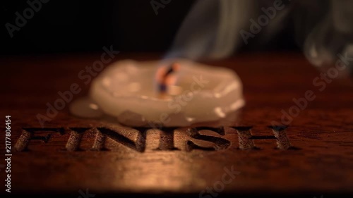 A melted candle stub with a smoking wick on a wooden surface carved with the word 