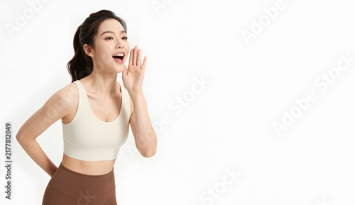 Elegant Asian female model with bright doe eyes, pale skin, small nose and plump lips, half-up hairstyle with soft waves, wearing a modern earth-tone gym ensemble in muted brown and cream