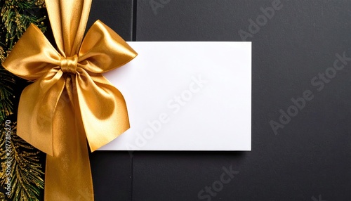 Gold gift bow with blank white card on dark background, decorated with festive Christmas tree branches for holiday season greetings.